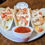 Three shrimp tacos on a plate with dipping sauce.