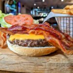 A bacon cheeseburger with fries on a wooden cutting board.