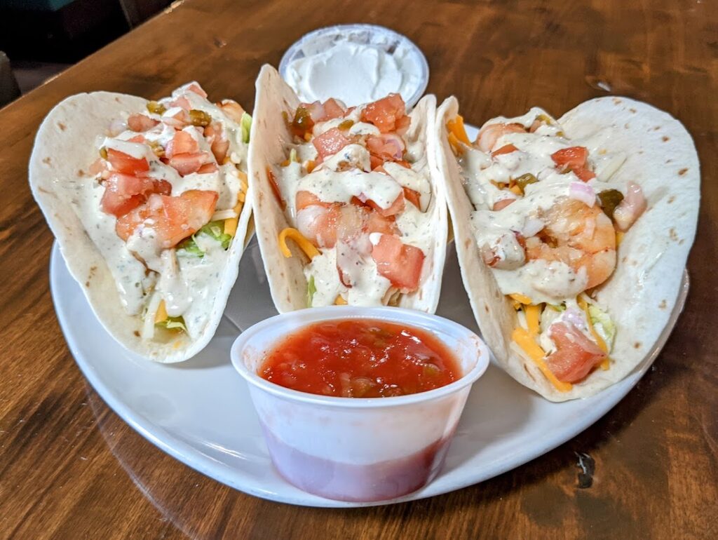 Three shrimp tacos on a plate with dipping sauce.