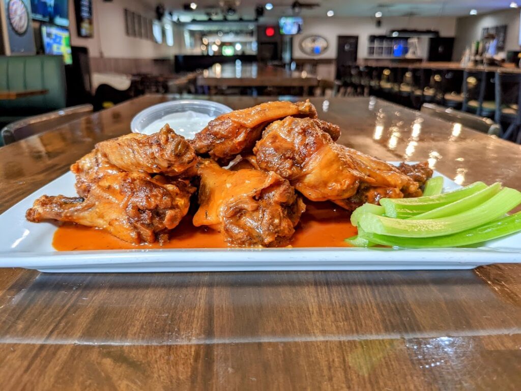 A plate of buffalo wings and celery on a wooden table.